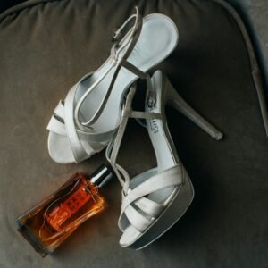 a pair of white high heeled shoes next to a bottle of perfume